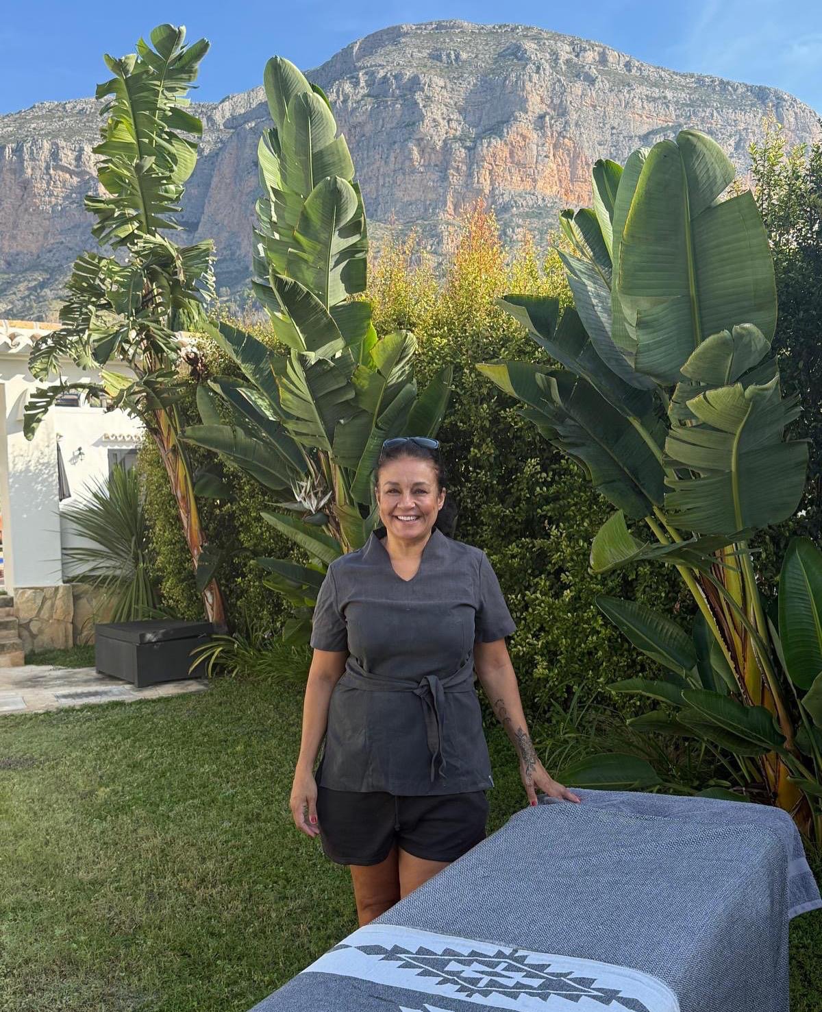 Lisa Blackie standing beside her massage table in a villa garden with Montgo mountain behind